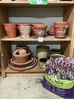 Terracotta pots of various sizes on wooden shelves with visible white mineral deposits and wear, includes stack of small saucers and multi-opening pot