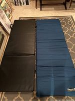 Thermarest camping mattress and black folding exercise mat side by side on carpeted floor.