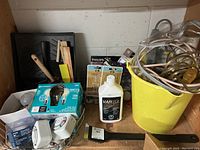 View of multiple utility items including light bulbs, painting tools, electrical timers, cords, and a bottle of Varsol.