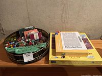 Overview of metal tin with marbles, playing card decks and two jigsaw puzzle boxes on wooden surface