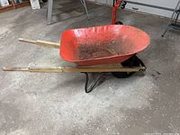 Side view of red metal wheelbarrow showing condition and wooden handles.