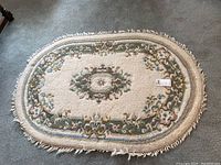 Top view of oval floral area rug with central medallion and fringed edges.