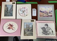Photo showing six matted art prints and collages arranged on a table, includes floral, architectural, landscape, and black and white sketch works.