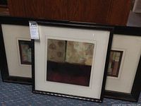 View of three framed abstract artworks leaning against a wooden surface showing size and framing