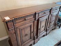 Full view of a dark stained wooden buffet with three drawers and three doors, showcasing detailed molding and metal ring handles.