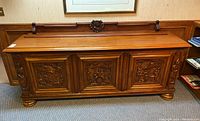 Front view of the large carved wood credenza showing the three carved panels of the doors and the bun feet.