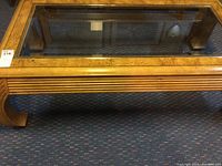 Top-front view of rectangular coffee table showing glass top and wooden frame and legs with a curved design.
