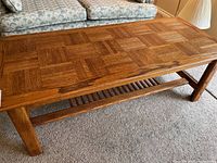 Full view of the rectangular parquet style wood coffee table in a living room setting showing legs and lower slatted shelf.