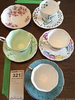 Five fine china tea cup and saucer pairs arranged on a wooden table with a MaxSold label.