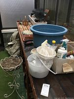 Image showing a large blue plastic planter pot, white buckets, and a decorative metal planter stand with soil or fiber material inside, set on a wooden table.