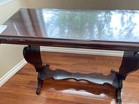 Full view of wood side table showing rectangular top, curved legs, and wavy stretcher support, placed on wood floor near wall.