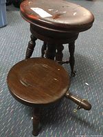 Photo showing both vintage wooden stools together on carpeted floor highlighting their size difference and wear.