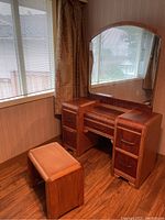 Photo showing the antique refinished wooden vanity dresser with attached mirror and matching upholstered bench in a corner near window and curtains.