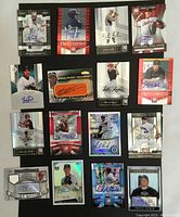 Photo of 16 baseball autograph cards arranged on a surface showing front with images and autographs.
