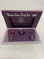 Full view of 1984 US Proof Set in purple cardboard sleeve with 'United States Proof Set 1984' text, showing five coins in display case.