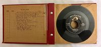 Photo of an open album sleeve showing a single 45 RPM vinyl record with RCA Victor label and a handwritten record index page.