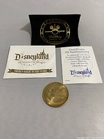 Photo showing the token, certificate of authenticity, and information card arranged together with the black velvet pouch behind them.