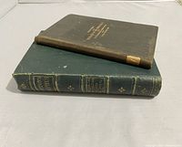 Two antique books stacked; green and black hardcovers, visible wear, spine damage on one