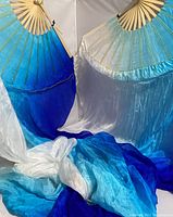 Photo showing two handheld folding fans with attached long flowing cloth in blue and white gradient colors on a plain background.
