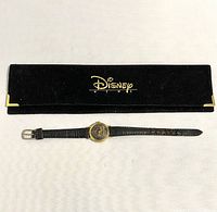 Black velvet pouch with gold Disney News logo and gold corner accents next to the Disneyland 35th Anniversary watch laid flat.