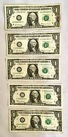 Full view of five US one-dollar bills with distinct serial numbers laid out flat.