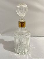 Clear ribbed glass decanter with matching ribbed bulbous stopper and a gold-tone collar at neck, photographed against white background from front