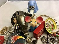 Photo showing assortment of vintage toys including Family Guy figurine, Snoopy, mouse figurine, red bus, and metal piggy bank along with jewelry and knick-knacks