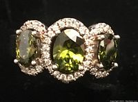 Close-up front view of ring showing three green oval stones surrounded by white CZ stones.
