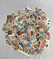 Wide view of a large pile of assorted US and international stamps arranged on a light background showing various designs and colors.