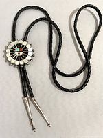 Full view of the bolo tie showing the braided leather cord, silver tips, and round Sun God pendant with colorful inlay.