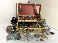 Full view of vintage jewelry box open with numerous assorted vintage costume jewelry pieces inside and outside of the box.