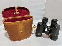 Brown leather case with strap and red interior embossed with 'Elite'. Case exterior shows wear and has a lock/pin closure.