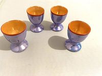 Photo of four lavender and orange lusterware cups arranged on a white surface showing side and angled views.