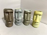 Front view of four tiki mugs showing Moai head designs and color variations