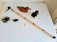 Lot items spread out on a white table showing walking stick and five bird and dog figurines.