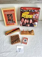 Overview photo showing all games arranged on a flat surface including the wooden block puzzle, Seinfeld Scene It game, dominoes, peg and ring wooden game, checkerboard, playing cards, and wooden discs.