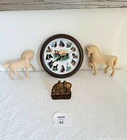 Front view of lot showing all four items: clock, two carved wooden horses, brass horse bookend