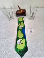 View of the golf collectible lot with necktie, two glass tumblers with metal golfer figures, wood carving of vintage golf club, and books