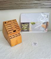 Wooden knife storage block with 23 slots and new plastic cutting board in packaging displayed on a white textured surface.
