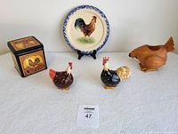Full display of all items on white tablecloth, showing six items: Portugal plate, wooden hen candle holder, two ceramic salt and pepper shakers, and metal tin.