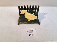 Front view of vintage cast iron letter holder showing yellow duck on green grass and picket fence background.