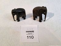 Two vintage ebony wood hand-carved elephant sculptures, one with missing eye and both missing trunks, approximately 3 inches tall each.