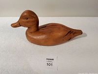 Side view of wooden duck decoy carving showing smooth natural wood finish and painted eye detail.