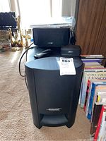 Full view of Bose subwoofer unit with remote control on top, surrounded by household items.
