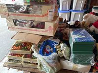Image of stacked boxes containing assorted Christmas ornaments and stationery items, some plastic wrapped, various colors.