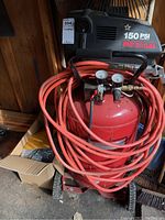 Front view of red air compressor unit with coiled red air hoses and pressure gauges on top, showing overall setup and condition