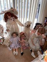 Wide shot of six dolls arranged seated and standing near window with vertical blinds
