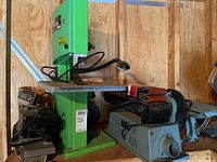 Overview of green Kawasaki band saw, black Craftsman belt sander and grey Delta belt sander on workshop shelf