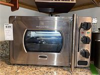 Front view of Wolfgang Puck stainless steel pressure oven showing the door with glass window and long handle.
