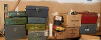 Stacked metal tool boxes in green, black, and red with boxes and various items alongside